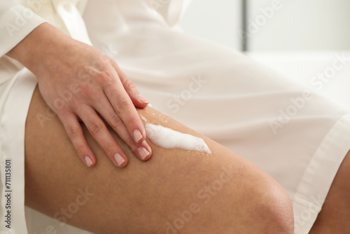 Woman applying self-tanning product onto leg indoors, closeup
