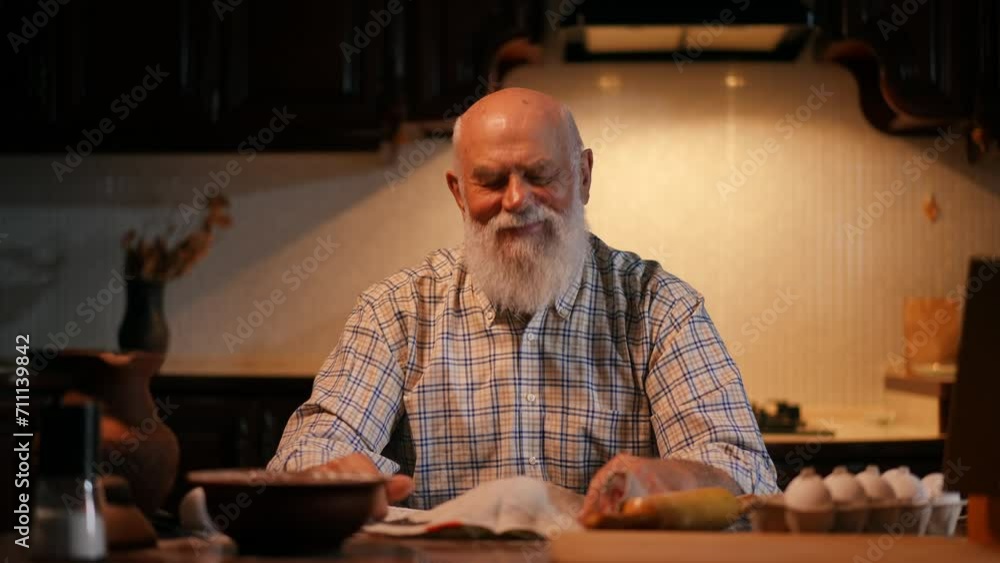 An elderly bearded man in a shirt covers freshly prepared dough with a towel. A man sits at a table in the kitchen in a modern home. The man smiles, pleased with the work done An elderly bearded man in a shirt covers freshly prepared dough with a towel. A man sits at a table in the kitchen in a modern home. The man smiles, pleased with the work done