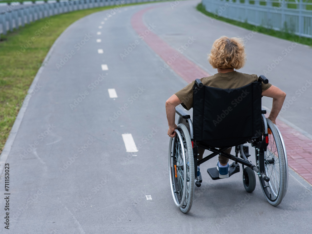 Rear view of an elderly woman in a wheelchair riding on a bike path. Rear view of an elderly woman in a wheelchair riding on a bike path.
