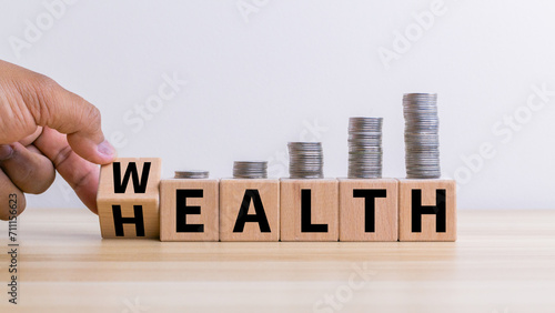 Hand flip wooden cube with word wealth to health with coins stack step up growing growth value. Investment in life insurance and healthcare concept