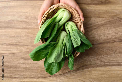 Bok choy or Pak choi (Chinese cabbage) in basket holding by hand on wooden background, Table top view photo