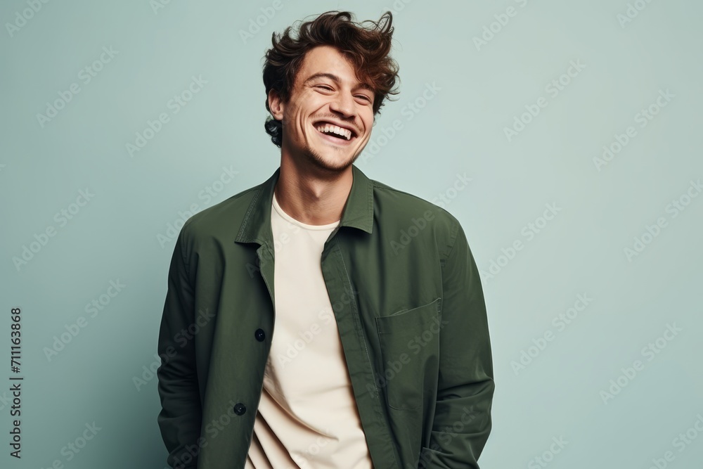 Handsome young man laughing and looking at camera while standing against blue background Handsome young man laughing and looking at camera while standing against blue background