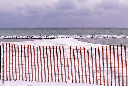 Photography Snow  fence (red)  on snow covered beach with rocks, lake ontario and clouds in