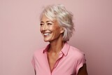 Happy mature woman looking at camera and smiling while standing against pink background