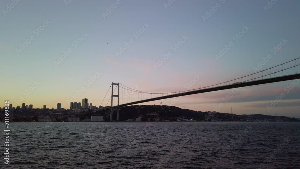 Evening, cinematic slow-mo, silhouette of Fatih Sultan Mehmet Bridge, Istanbul European side from a ferry on Bosphorus. Bridge, city create silhouette against backdrop of setting sun final rays. Evening, cinematic slow-mo, silhouette of Fatih Sultan Mehmet Bridge, Istanbul European side from a ferry on Bosphorus. Bridge, city create silhouette against backdrop of setting sun final rays.