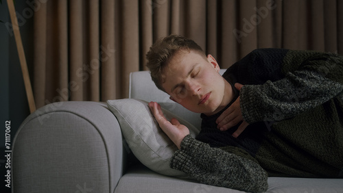 Side shot of blonde man suddenly wakes up while sleeping on sofa at home due to anxiety, disorder, bad dreams and illness or disease 