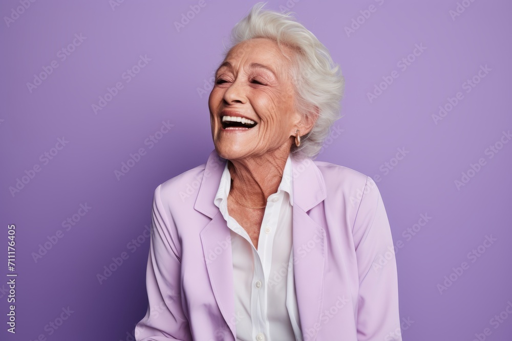 Happy senior woman laughing and looking at camera while standing against purple background Happy senior woman laughing and looking at camera while standing against purple background