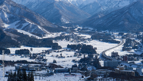 Panoramic view of a quaint town nestled in a valley with snow-covered fields and surrounding mountain peaks.