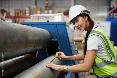 female factory worker using tape measure and measuring the length of the steel pipe in the factory photo