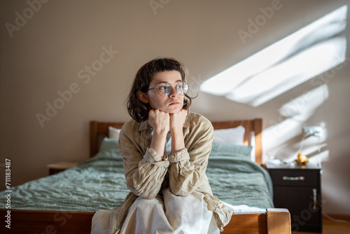 Depressed lonely woman sitting on cozy bed sadly look at window feeling anxiety. Alone girl suffering from emotional pain having life troubles, problems. Mental disorder anhedonia, stress discomfort photo