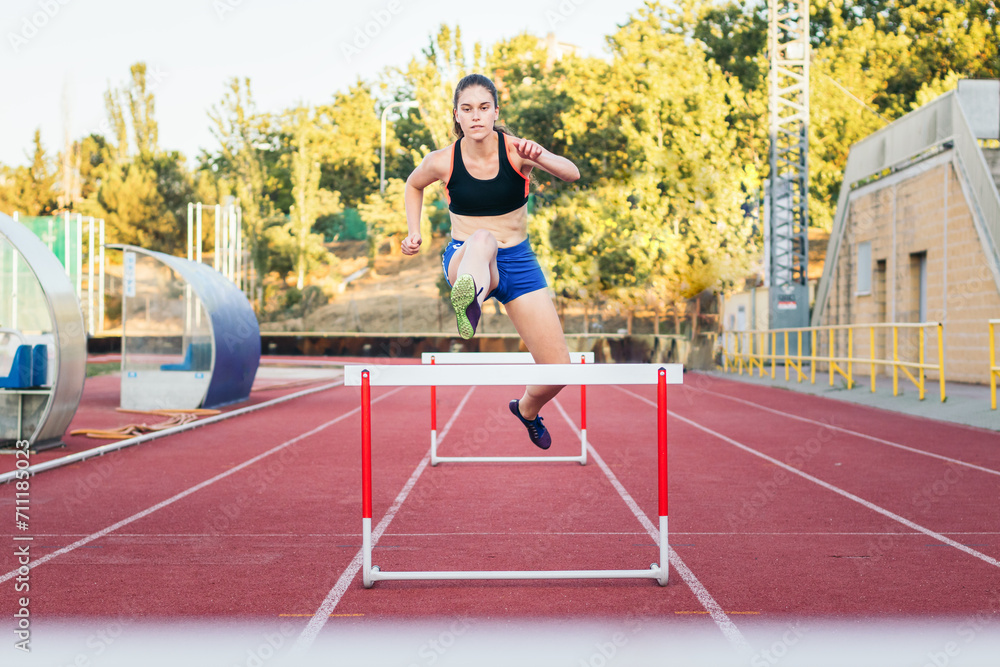 An athletic woman jumping hurdles on an athletics track.