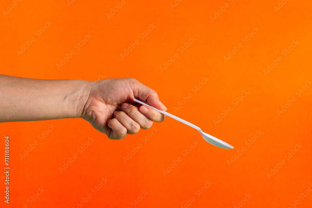 White plastic spoon in hand on orange background White plastic spoon in hand on orange background
