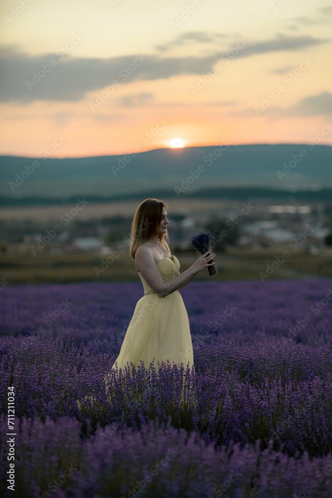 Woman poses in lavender field at sunset. Happy woman in yellow dress holds lavender bouquet. Aromatherapy concept, lavender oil, photo session in lavender Woman poses in lavender field at sunset. Happy woman in yellow dress holds lavender bouquet. Aromatherapy concept, lavender oil, photo session in lavender