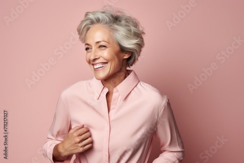 Smiling senior woman in pink shirt looking at camera over pink background