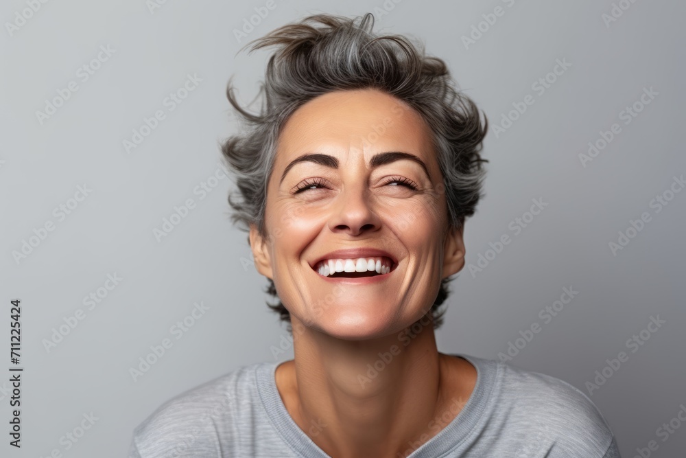 Portrait of a happy middle-aged woman laughing against grey background Portrait of a happy middle-aged woman laughing against grey background