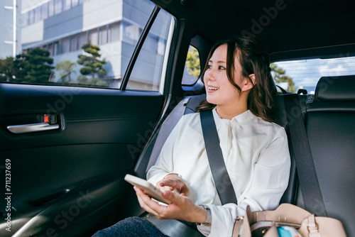 スマホを持ちながら自動車の後部座席で窓の外を眺めるビジネスウーマン（出張・検索・アプリ）
 photo