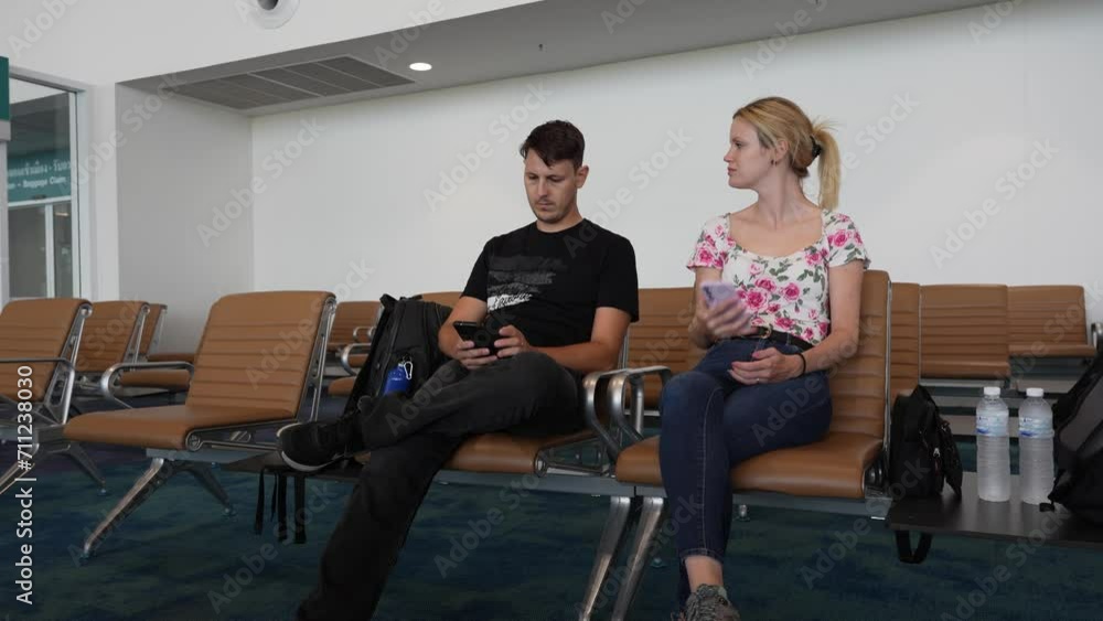 A young couple waits in the airport lounge for their departure and checks their cell phone. A young couple waits in the airport lounge for their departure and checks their cell phone.