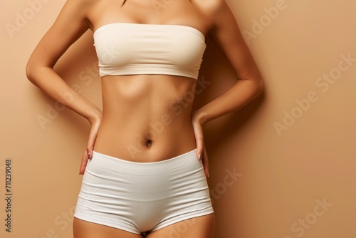 Young woman with flat belly on beige background, closeup. Plastic surgery concept photo