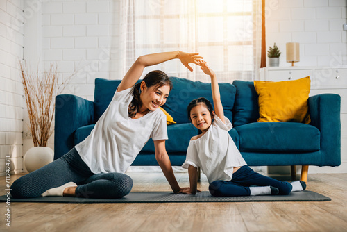 A mother coaches her little daughter in yoga creating a family bond filled with happiness relaxation and togetherness. Their smiles reflect joy and vitality in their domestic life. photo