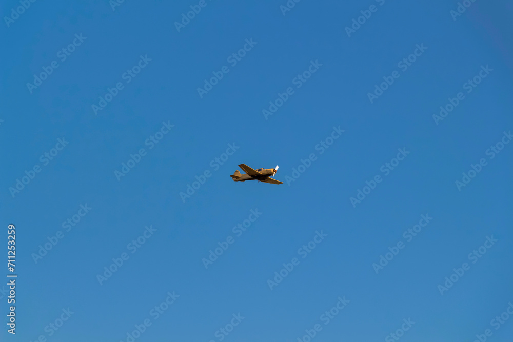 A sporty orange airplane against a clear blue sky.