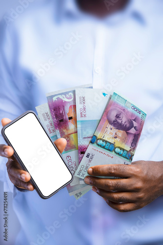 Black person holding Cape Verdean Escudo notes and showing phone with blank screen to the camera. Hand holding Cape Verdean currency notes, 3d rendered money photo