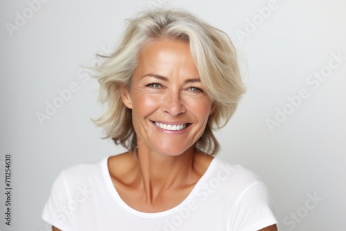 Closeup portrait of a happy mature woman smiling against grey background.
