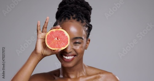 Grapefruit, beauty and face of happy woman in studio for vitamin c benefits, detox or glow on grey background. Portrait, african model or laugh with citrus fruits for skincare, sustainability or diet photo