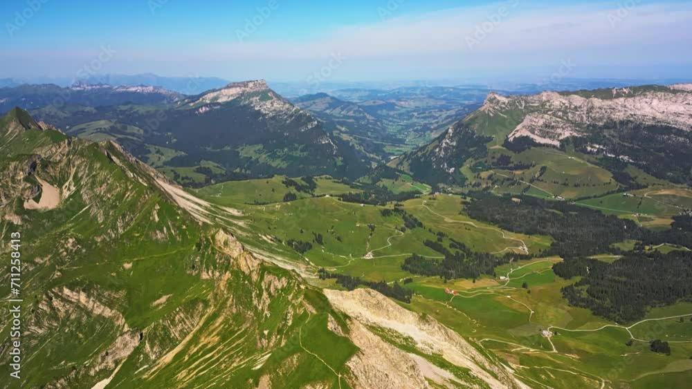 Aerial view of a vast mountain range and a blue sky, than pans down to reveal a high peak that slopes down to a valley Aerial view of a vast mountain range and a blue sky, than pans down to reveal a high peak that slopes down to a valley