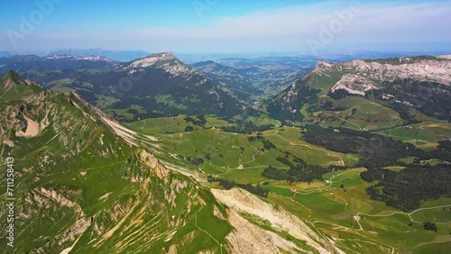 Aerial view of a vast mountain range and a blue sky, than pans down to reveal a high peak that slopes down to a valley photo