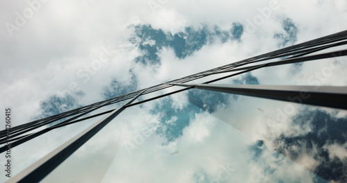 Low angle, skyscraper building and clouds in city with reflection, nature and urban infrastructure. Architecture, cityscape and skyline and metro with landscape, glass and sky background in timelapse