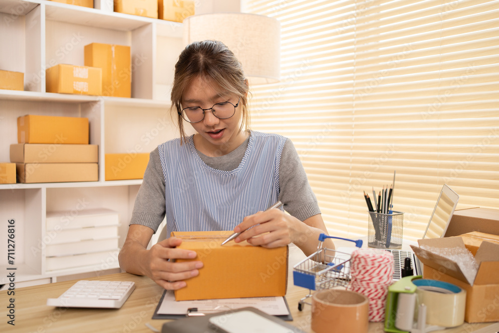 Sell products online, Woman is writing down the customer's details and addresses on box in order to prepare for shipping according to the information, Packing box, Sell online. Sell products online, Woman is writing down the customer's details and addresses on box in order to prepare for shipping according to the information, Packing box, Sell online.