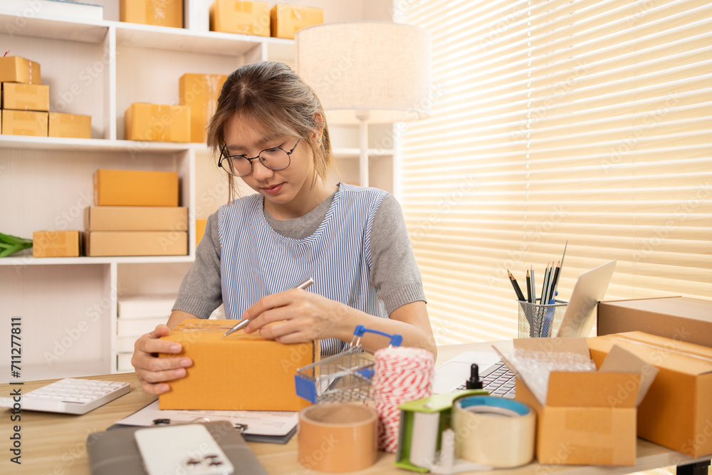 Sell products online, Woman is writing down the customer's details and addresses on box in order to prepare for shipping according to the information, Packing box, Sell online. Sell products online, Woman is writing down the customer's details and addresses on box in order to prepare for shipping according to the information, Packing box, Sell online.