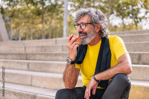 senior sports man rests eating an apple after a hard workout, concept of healthy and active lifestyle in the middle age, copy space for text