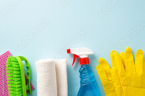 Embrace cleanliness with household items. Top-down view of cleaning supplies—brush, gloves, spray, rugs—on a muted blue background. Perfect for text or promotions photo