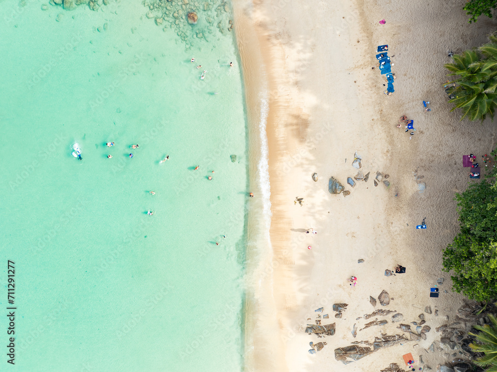View from above, stunning aerial view of Banana beach, a beautiful white sand beach surrounded by palm trees and bathed by a turquoise water. Phuket, Thailand.