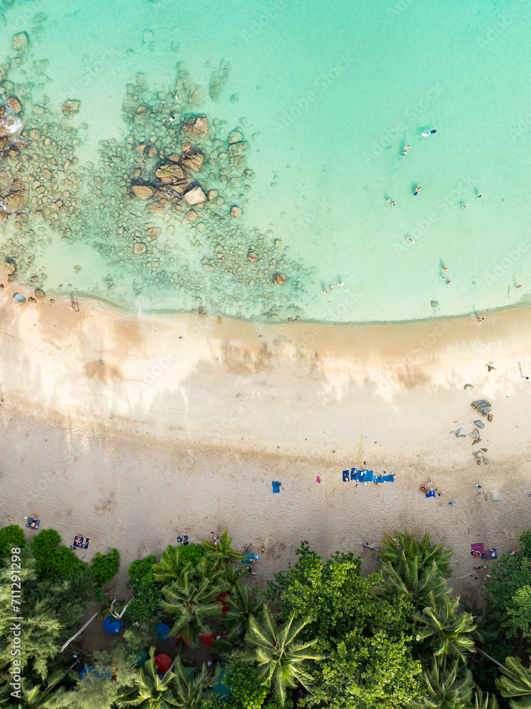 View from above, stunning aerial view of Banana beach, a beautiful white sand beach surrounded by palm trees and bathed by a turquoise water. Phuket, Thailand.