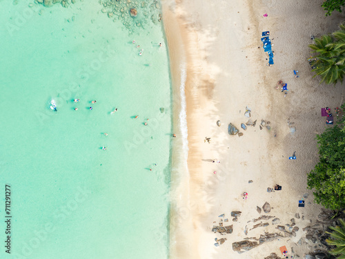 View from above, stunning aerial view of Banana beach, a beautiful white sand beach surrounded by palm trees and bathed by a turquoise water. Phuket, Thailand.