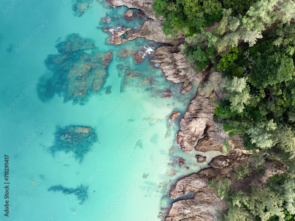 View from above, stunning aerial view of a rocky coastline surrounded by palm trees and bathed by a turquoise water. Phuket, Thailand.