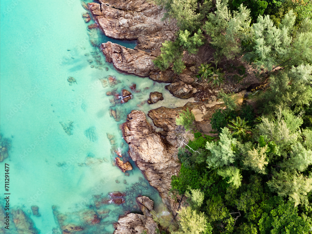 View from above, stunning aerial view of a rocky coastline surrounded by palm trees and bathed by a turquoise water. Phuket, Thailand.