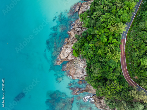 Obraz na płótnie View from above, stunning aerial view of a road that runs alongside a rocky coastline surrounded by palm trees and bathed by a turquoise water. Phuket, Thailand. w salonie