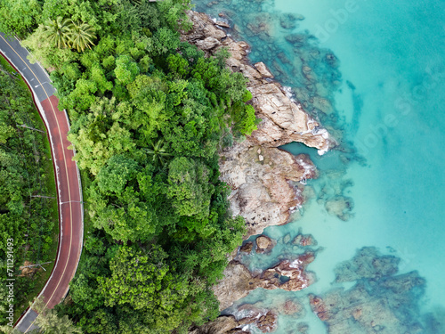 Obraz na płótnie View from above, stunning aerial view of a road that runs alongside a rocky coastline surrounded by palm trees and bathed by a turquoise water. Phuket, Thailand. w salonie