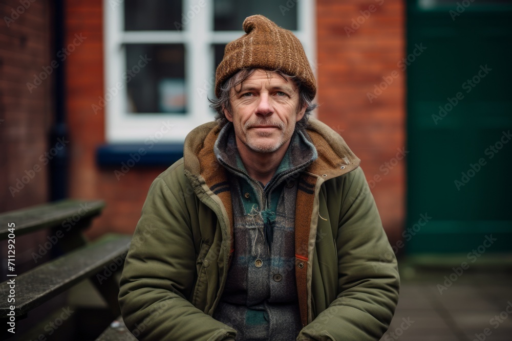 Handsome middle-aged man in warm clothes and a knitted hat is sitting on a bench in the city. Handsome middle-aged man in warm clothes and a knitted hat is sitting on a bench in the city.
