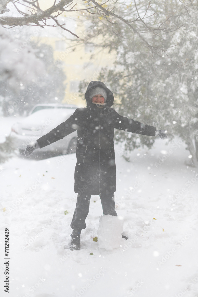 a girl is playing with snow on the street, it is snowing, a blizzard and frost on a winter day a girl is playing with snow on the street, it is snowing, a blizzard and frost on a winter day