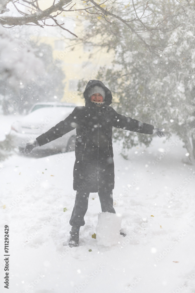 a girl is playing with snow on the street, it is snowing, a blizzard and frost on a winter day