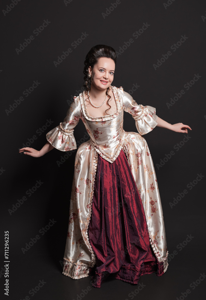Beautiful smiling woman in rococo style medieval dress standing against dark background