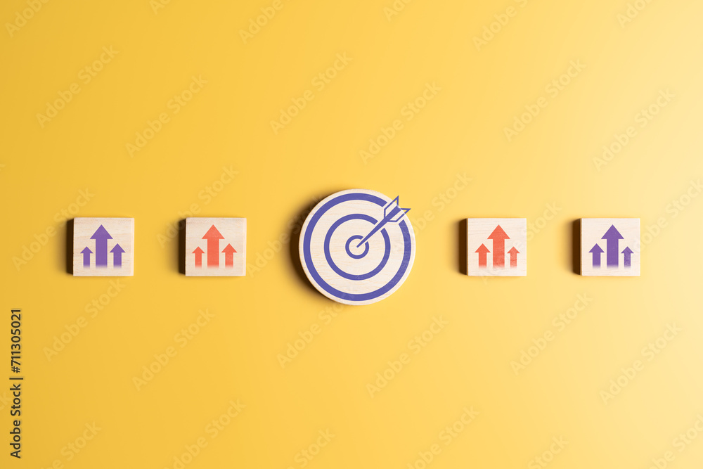 Business growth success achievement concept. Arranging wooden blocks with arrow up icons and target dartboard in circle on a yellow scene. Planning and development leadership for customer targeted.