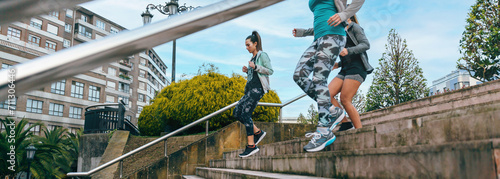 Group of happy young women friends training running down stairs in town