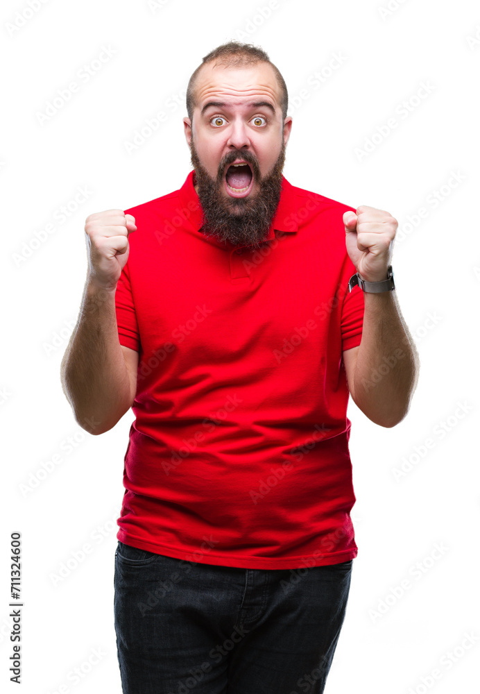 Young caucasian hipster man wearing red shirt over isolated background celebrating surprised and amazed for success with arms raised and open eyes. Winner concept. Young caucasian hipster man wearing red shirt over isolated background celebrating surprised and amazed for success with arms raised and open eyes. Winner concept.