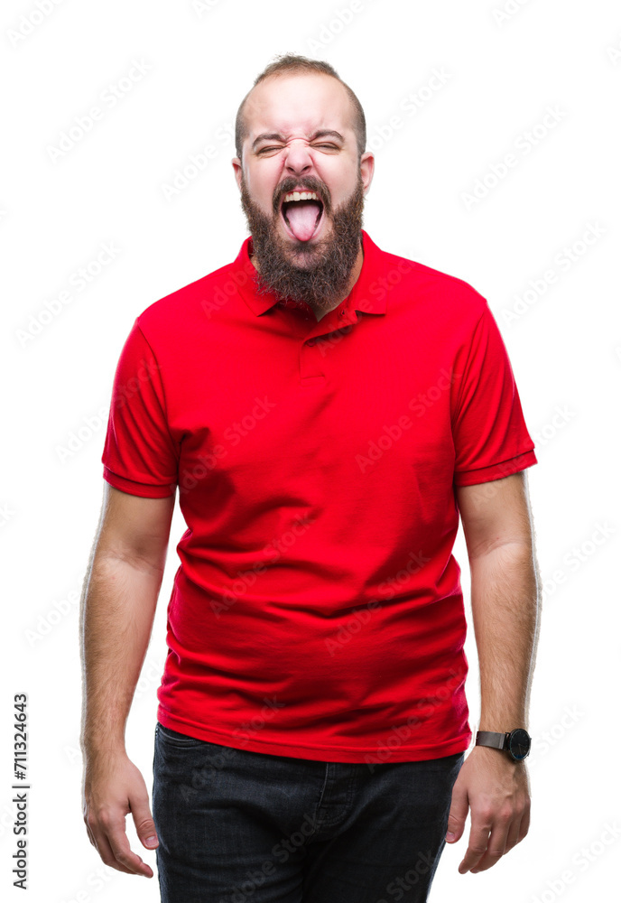 Young caucasian hipster man wearing red shirt over isolated background sticking tongue out happy with funny expression. Emotion concept. Young caucasian hipster man wearing red shirt over isolated background sticking tongue out happy with funny expression. Emotion concept.