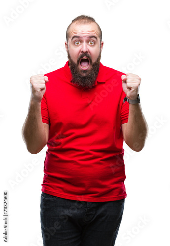 Young caucasian hipster man wearing red shirt over isolated background celebrating surprised and amazed for success with arms raised and open eyes. Winner concept.